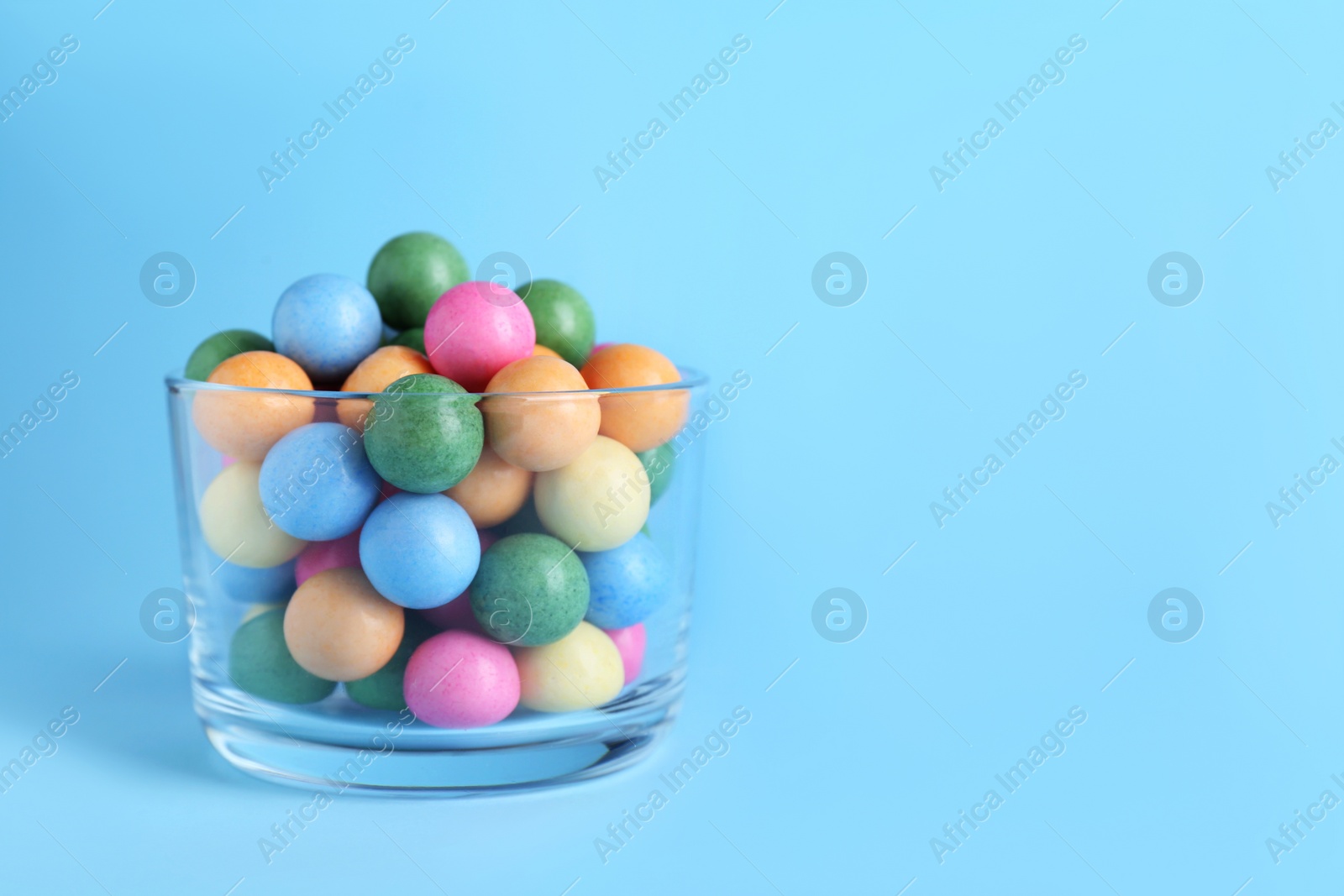 Photo of Bowl with bright gumballs on light blue background. Space for text