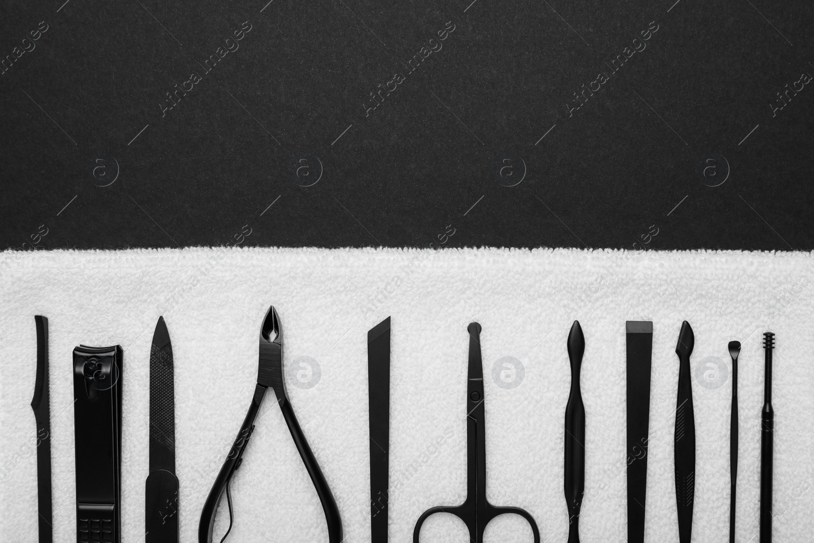 Photo of Towel with set of manicure tools on black background, top view. Space for text