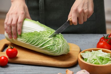 Photo of Woman cutting fresh chinese cabbage at grey wooden table in kitchen, closeup