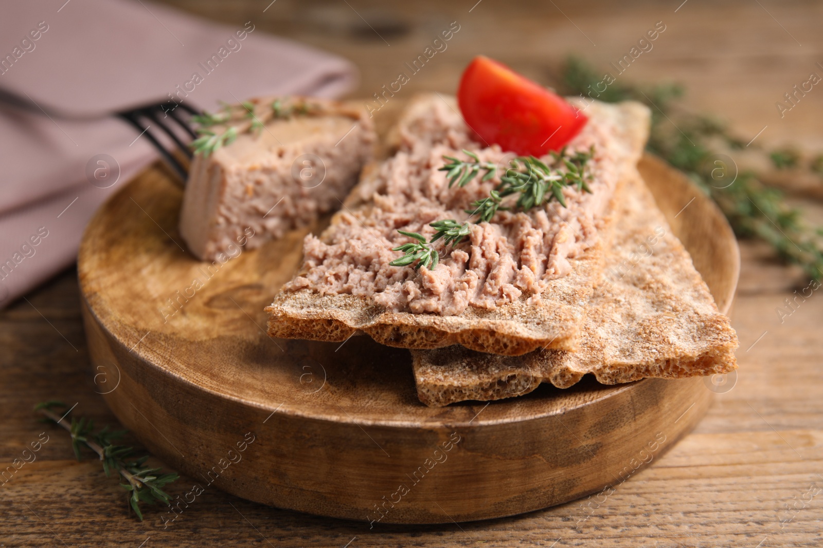 Photo of Crispy crackers with delicious meat pate and thyme served on wooden table, closeup