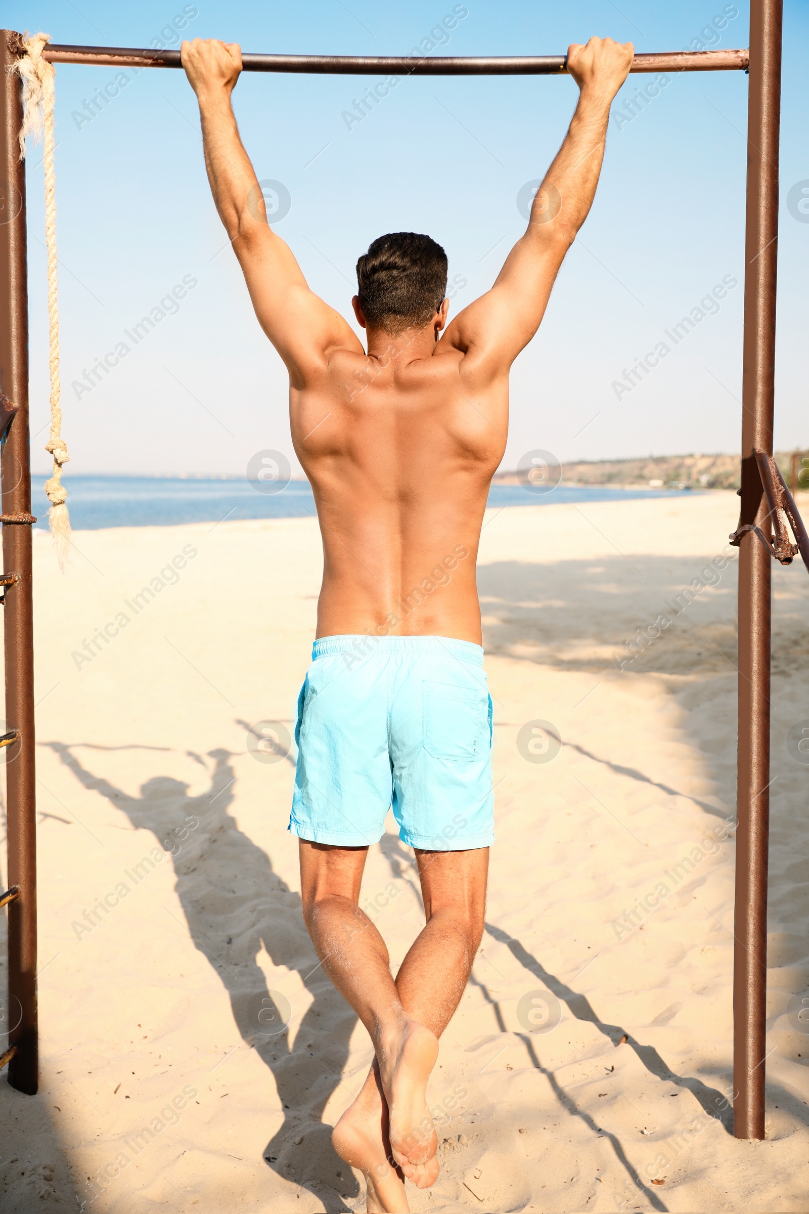 Photo of Man with slim body doing pull-ups
on beach