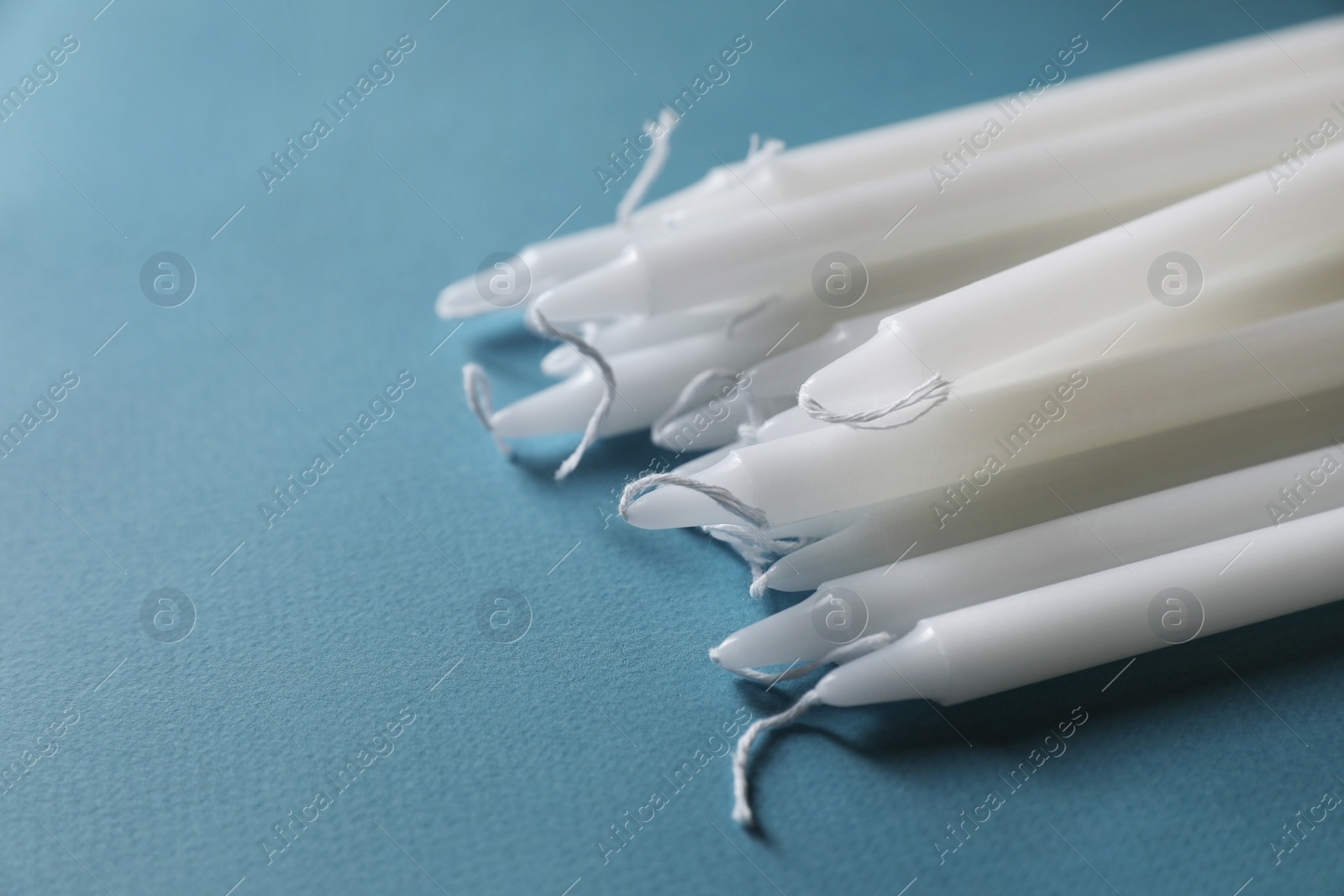 Photo of Many church wax candles on light blue background, closeup. Space for text