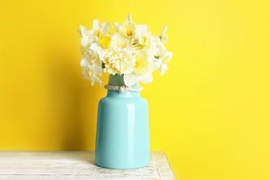 Bouquet of daffodils in vase on table against color background, space for text. Fresh spring flowers