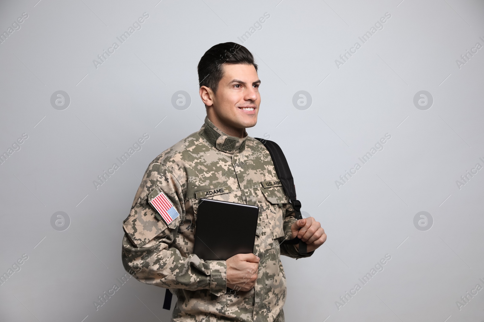 Photo of Cadet with backpack and tablet on light grey background. Military education