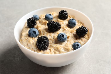 Photo of Tasty oatmeal porridge with blackberries and blueberries in bowl on grey table