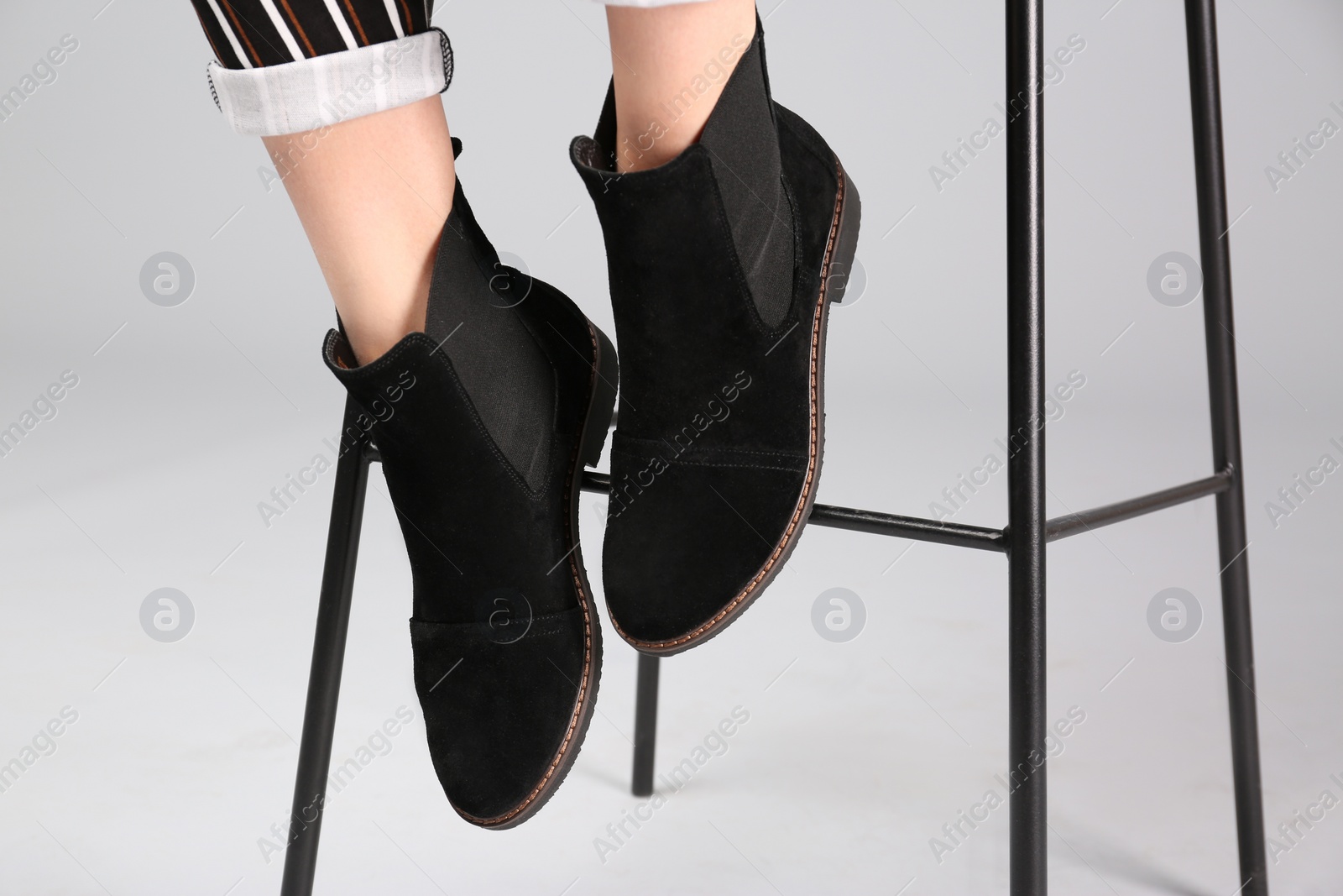 Photo of Woman in trendy shoes sitting on bar stool, light background