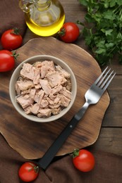 Bowl with canned tuna and products on wooden table, flat lay