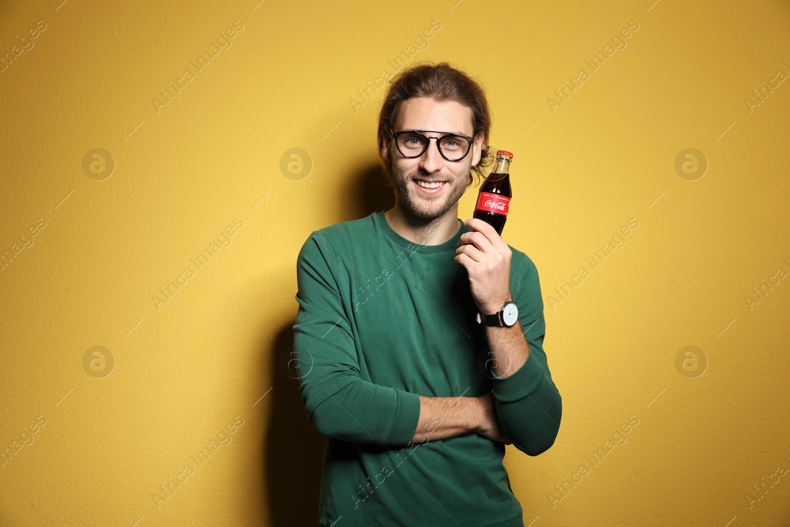 Photo of MYKOLAIV, UKRAINE - NOVEMBER 28, 2018: Young man with bottle of Coca-Cola on color background