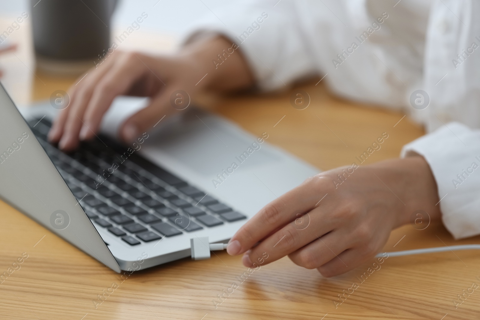 Photo of Woman connecting charger cable to laptop at wooden table, closeup