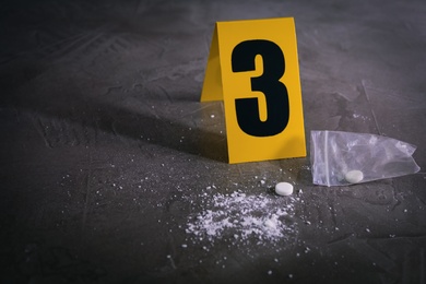Pill and white powder near crime scene marker on grey stone table, space for text