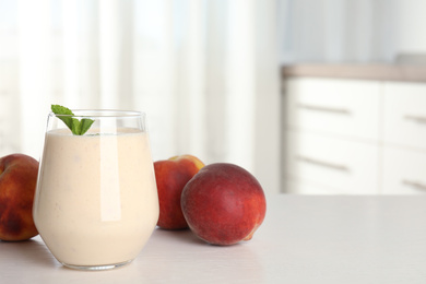 Photo of Tasty milk shake and fresh peaches on white table. Space for text