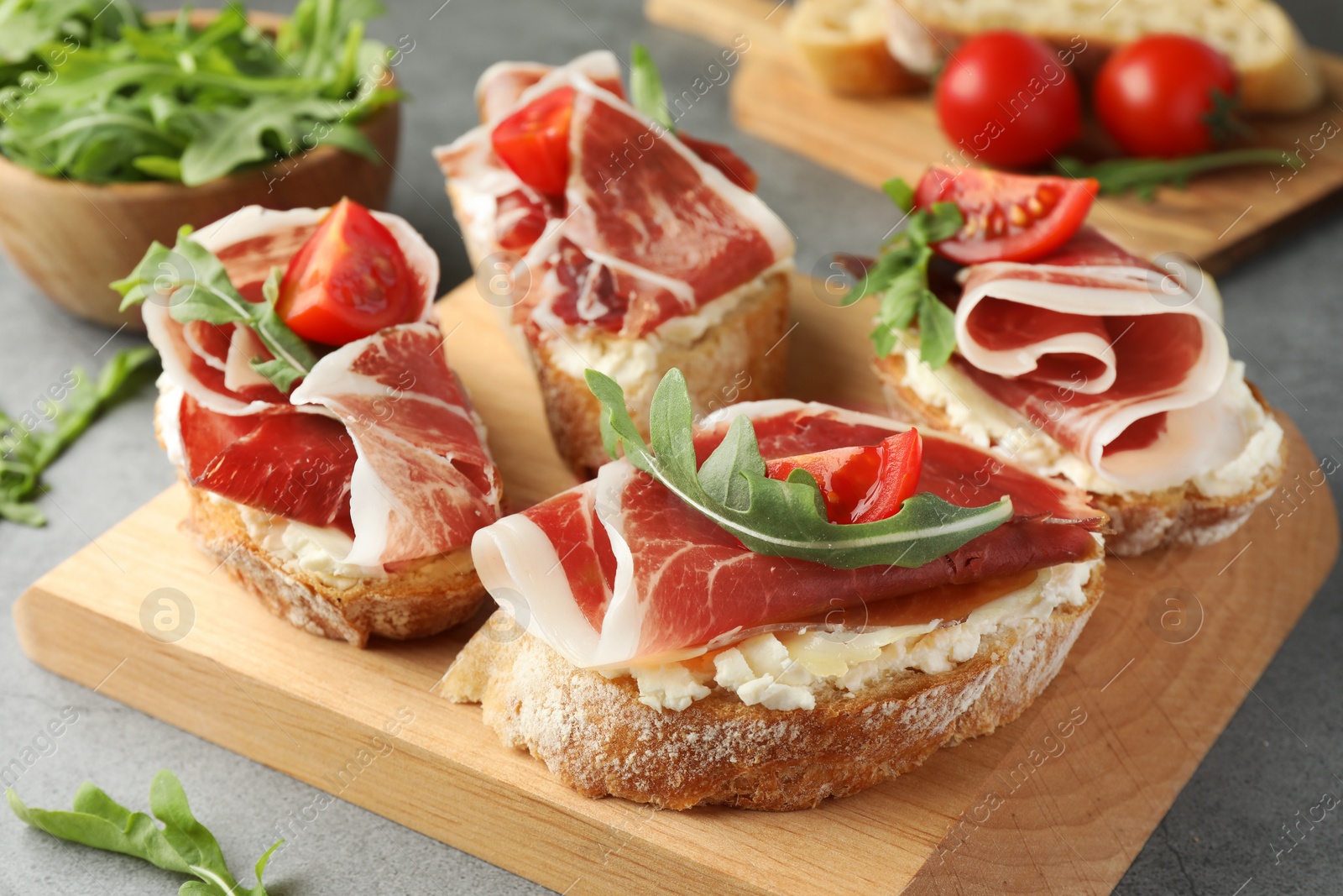 Photo of Tasty sandwiches with cured ham, tomatoes and arugula on grey table, closeup