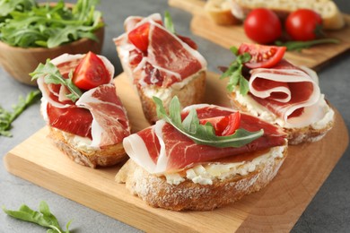 Tasty sandwiches with cured ham, tomatoes and arugula on grey table, closeup