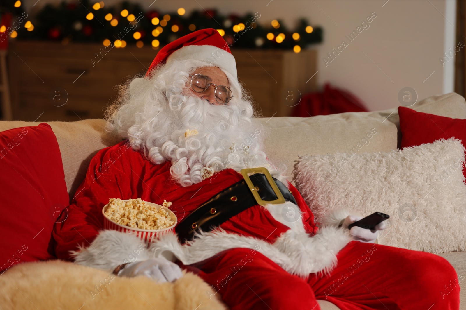 Photo of Merry Christmas. Santa Claus with popcorn bucket sleeping while watching TV on sofa at home