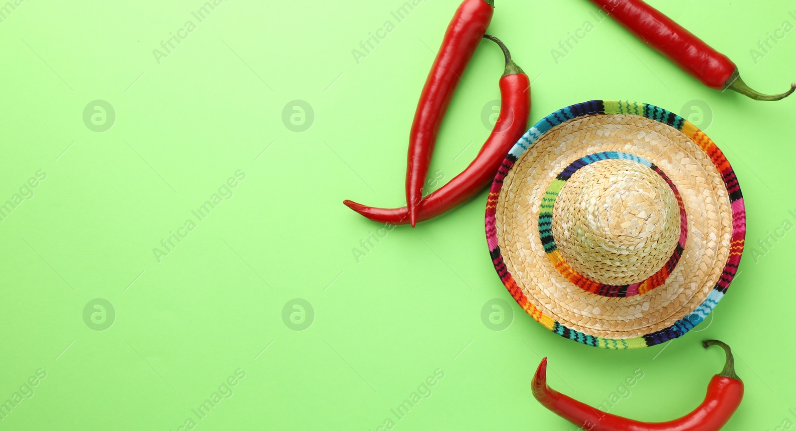 Photo of Mexican sombrero hat and chili peppers on green background, flat lay. Space for text