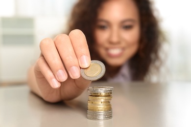 Young African-American woman stacking coins at table, focus on hand