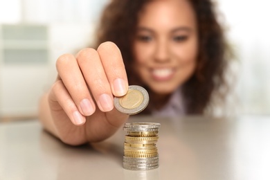 Photo of Young African-American woman stacking coins at table, focus on hand