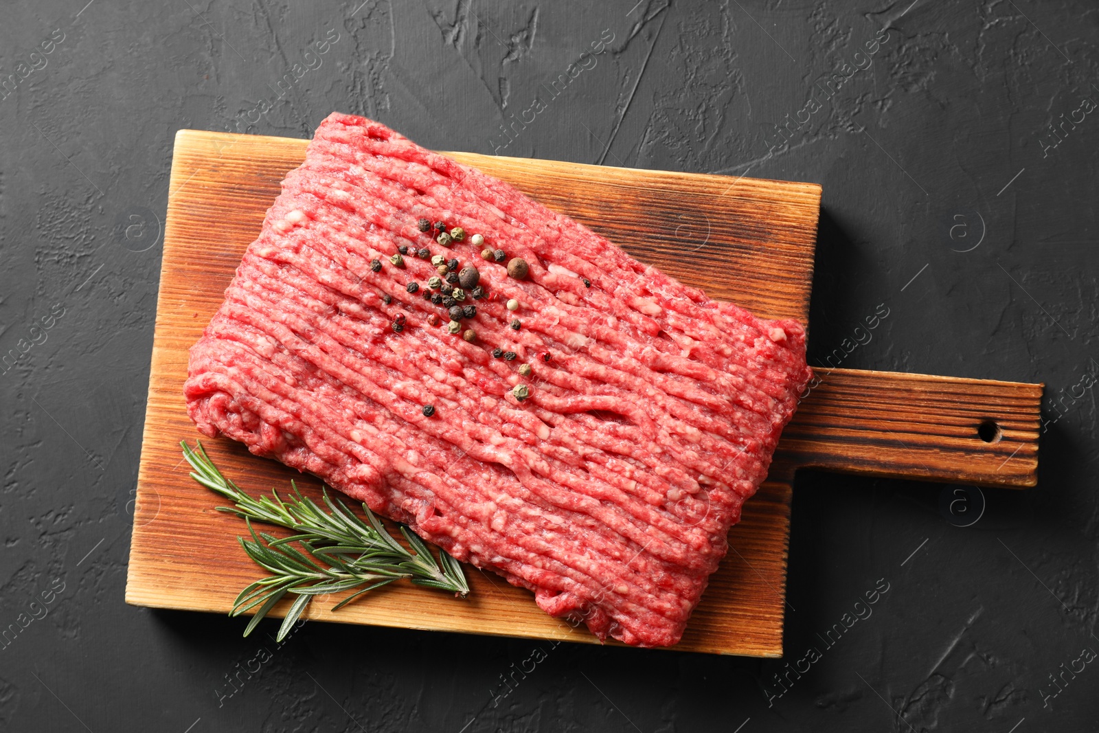 Photo of Raw ground meat, rosemary and peppercorns on black table, top view