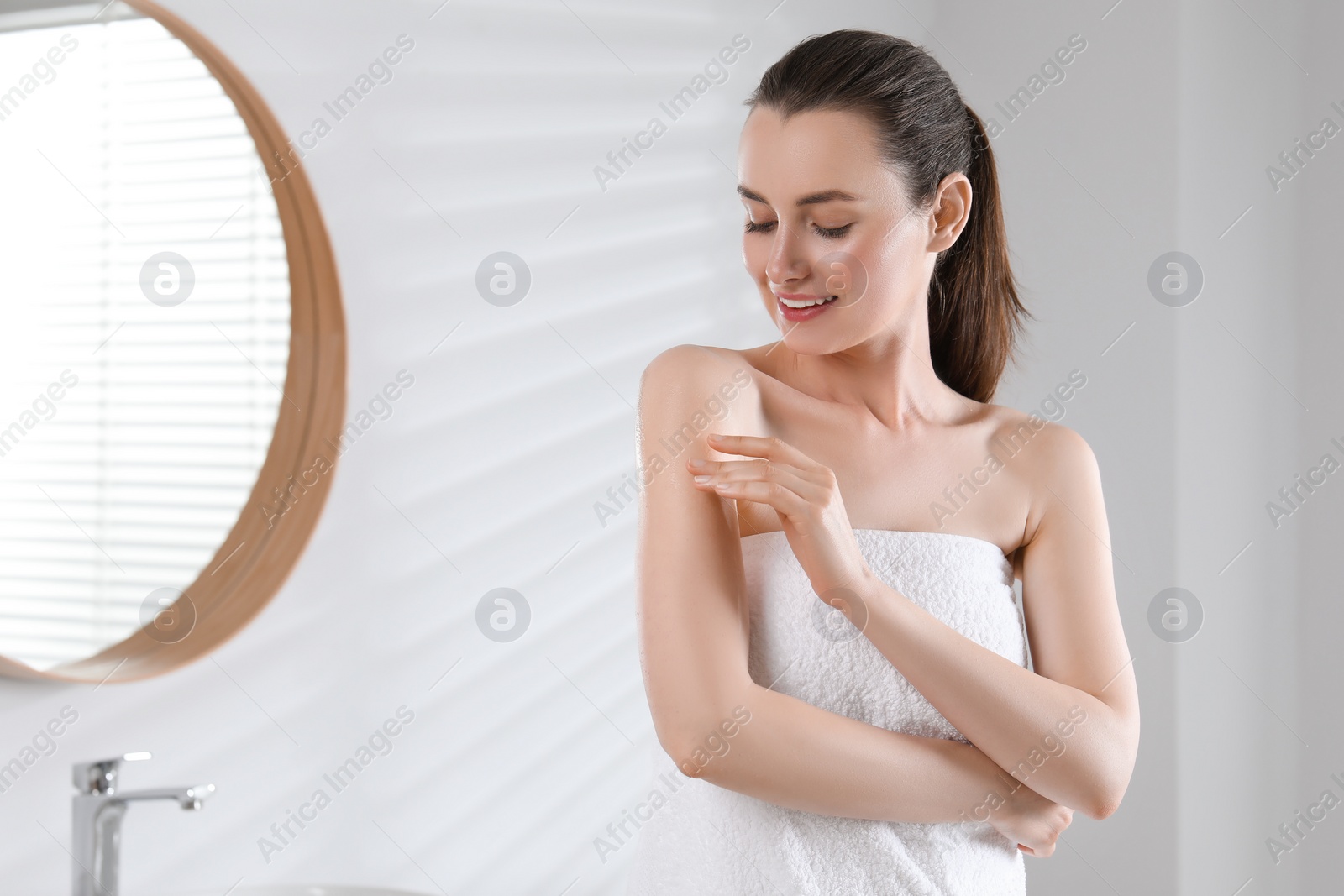Photo of Happy woman applying body oil onto arm in bathroom, space for text
