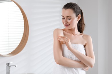 Happy woman applying body oil onto arm in bathroom, space for text