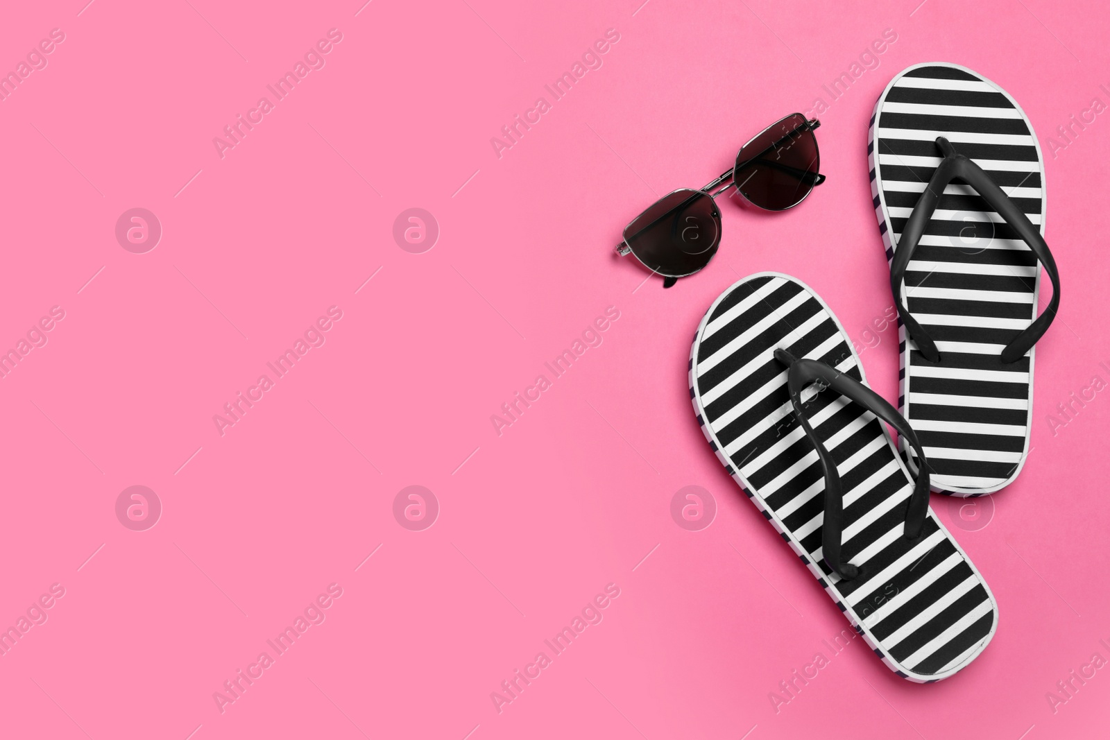 Photo of Stylish flip flops and sunglasses on pink background, flat lay. Space for text