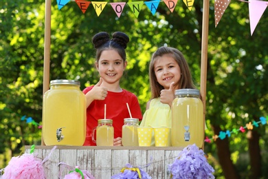 Photo of Cute little girls at lemonade stand in park. Summer refreshing natural drink