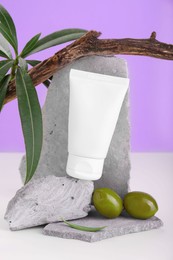 Photo of Tube of natural cream and olives on stones against purple background