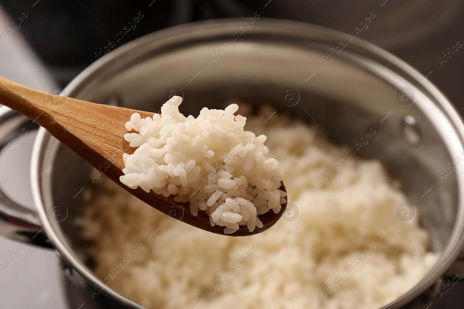 Photo of Wooden spoon with delicious rice over pot, closeup