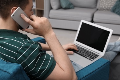 Photo of Young man working with laptop on armchair in home office