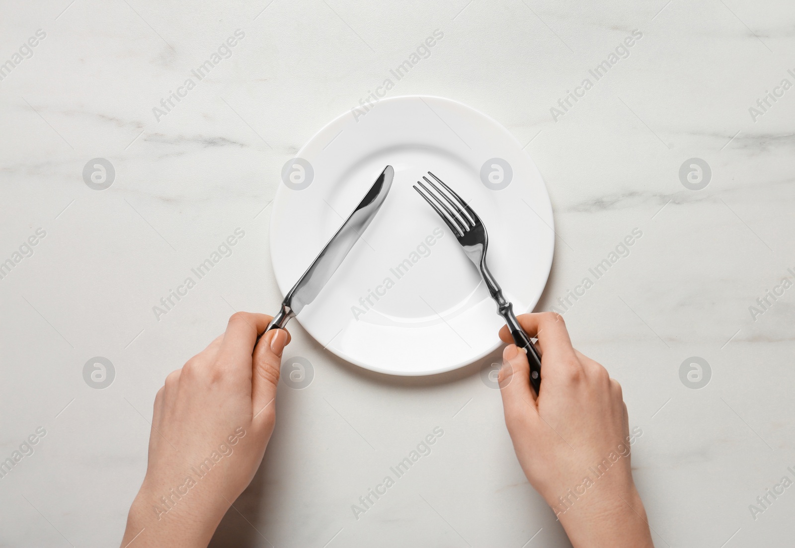 Photo of Woman with empty plate and cutlery at white marble table, top view