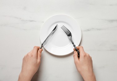 Woman with empty plate and cutlery at white marble table, top view