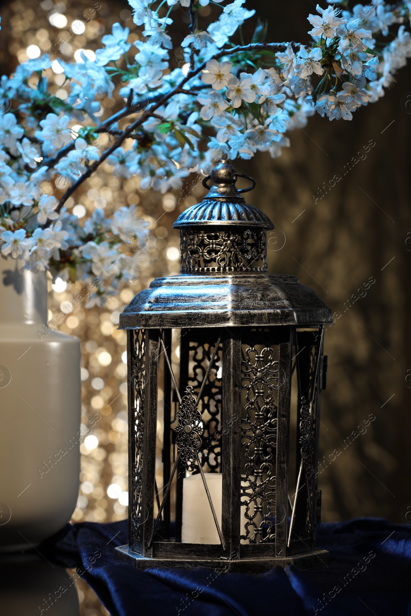 Photo of Arabic lantern and vase with flowers on table against blurred lights
