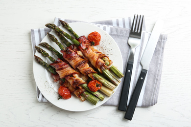 Photo of Oven baked asparagus wrapped with bacon on white wooden table, flat lay