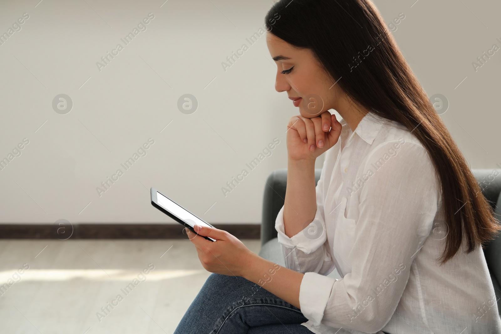 Photo of Young woman using e-book reader at home, space for text