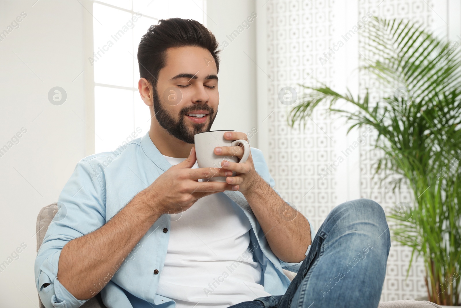 Photo of Young man with cup of drink relaxing at home