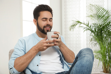 Young man with cup of drink relaxing at home
