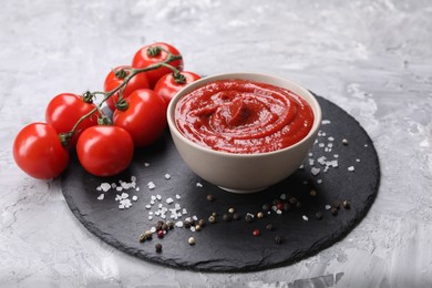 Organic ketchup in bowl, fresh tomatoes and spices on grey textured table. Tomato sauce