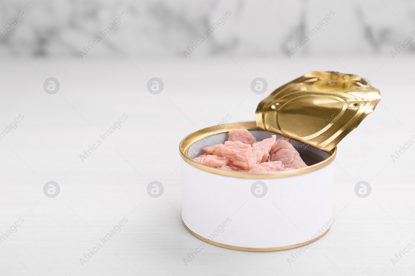 Photo of Tin can with canned tuna on white table, closeup. Space for text