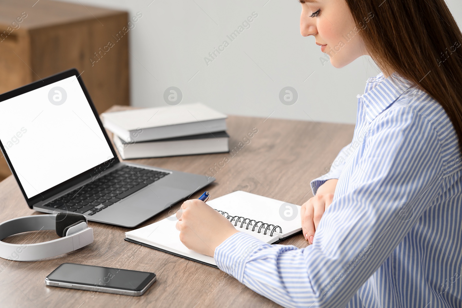 Photo of E-learning. woman taking notes during online lesson at table indoors