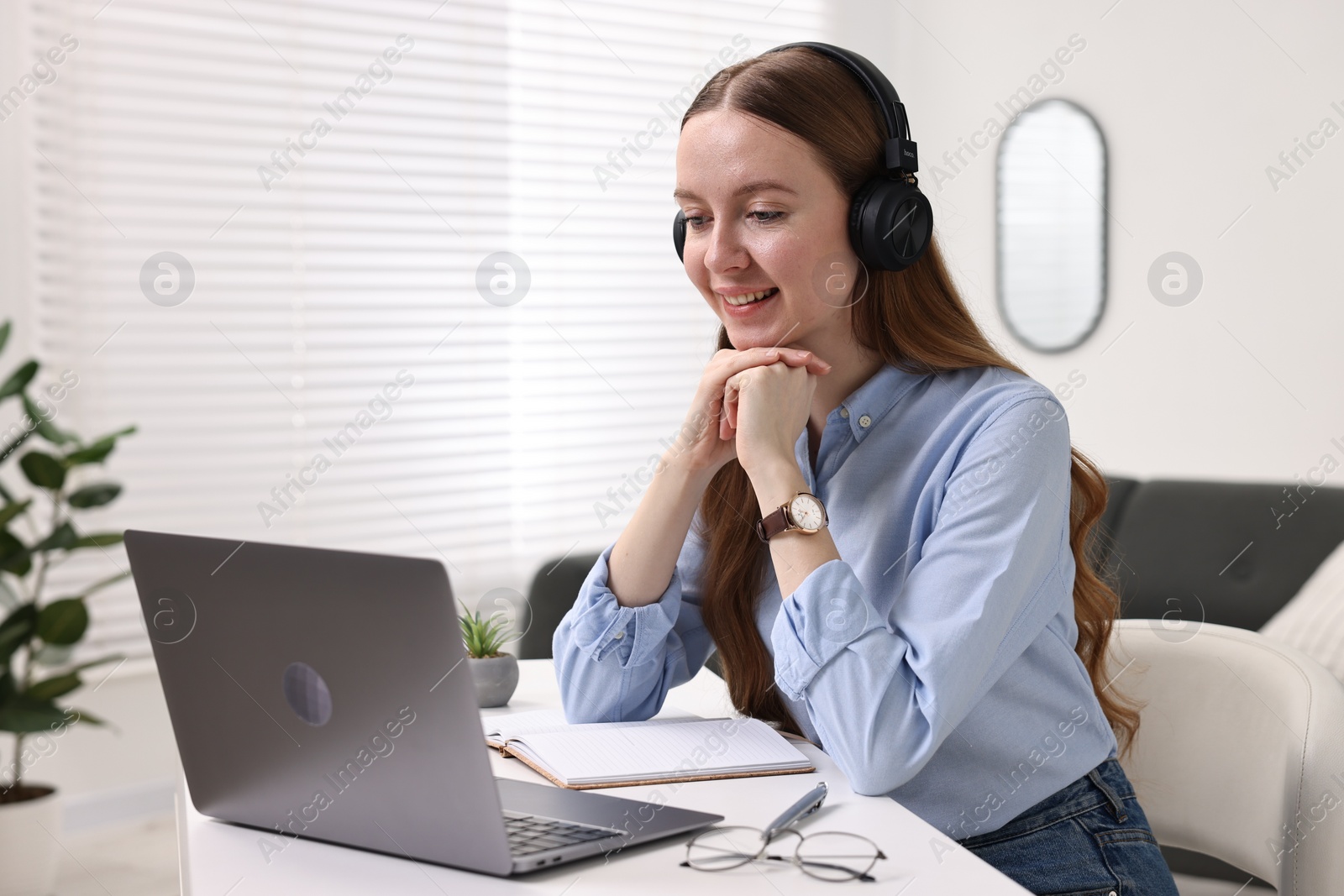 Photo of E-learning. Young woman using laptop during online lesson at white table indoors