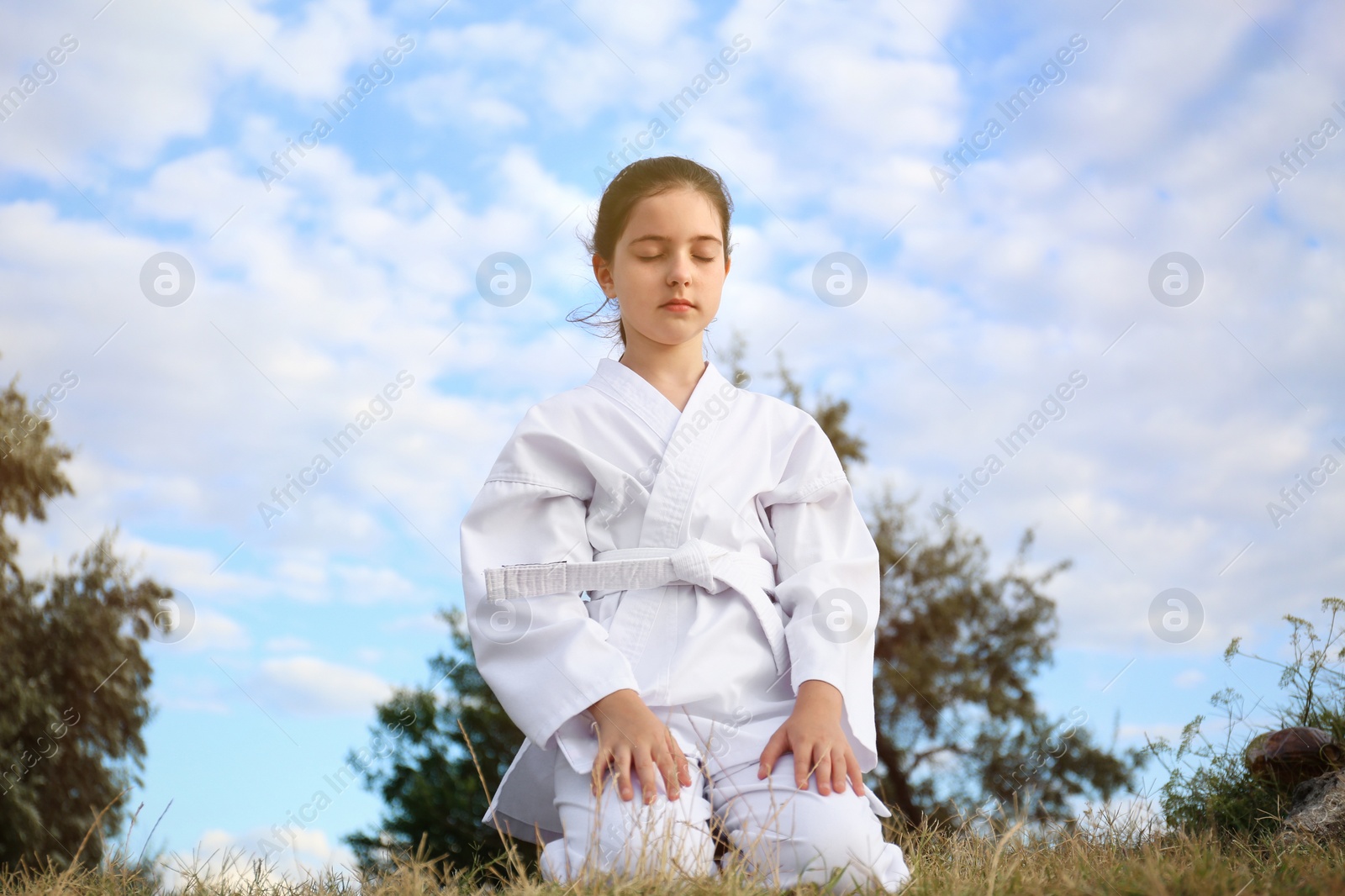 Photo of Cute little girl in kimono meditating outdoors. Karate practicing