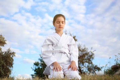 Cute little girl in kimono meditating outdoors. Karate practicing