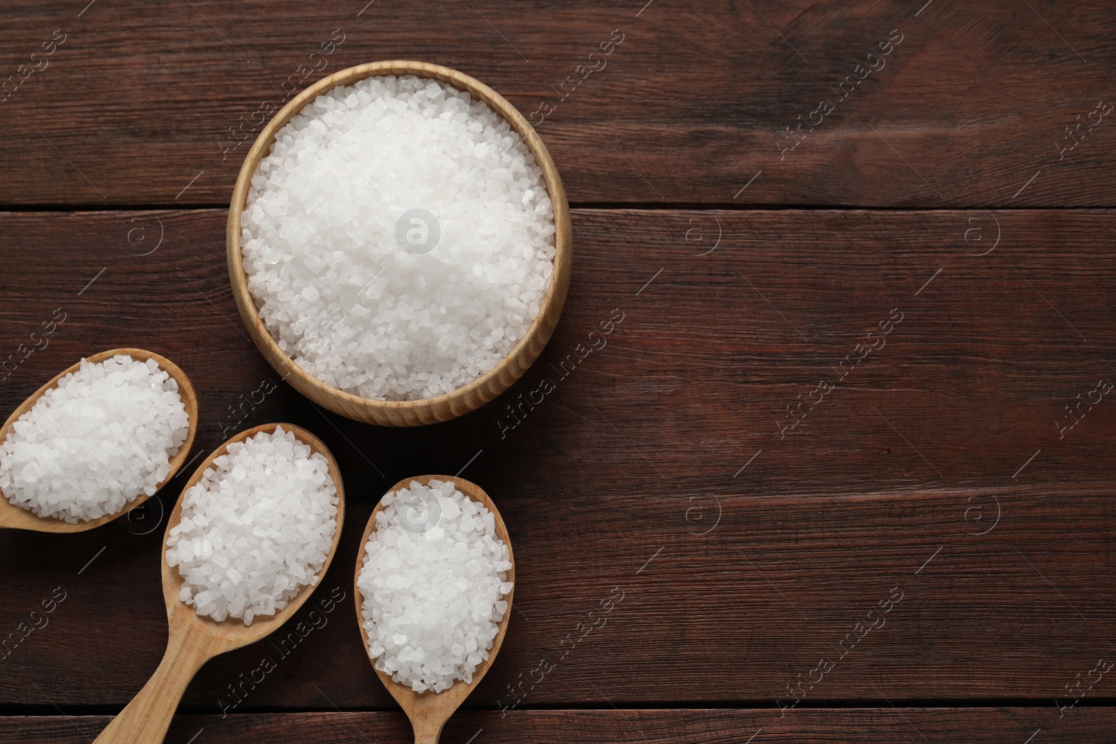 Photo of Bowl and spoons with natural sea salt on wooden table, flat lay. Space for text