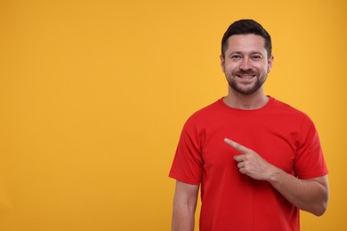 Photo of Special promotion. Smiling man pointing at something on orange background. Space for text