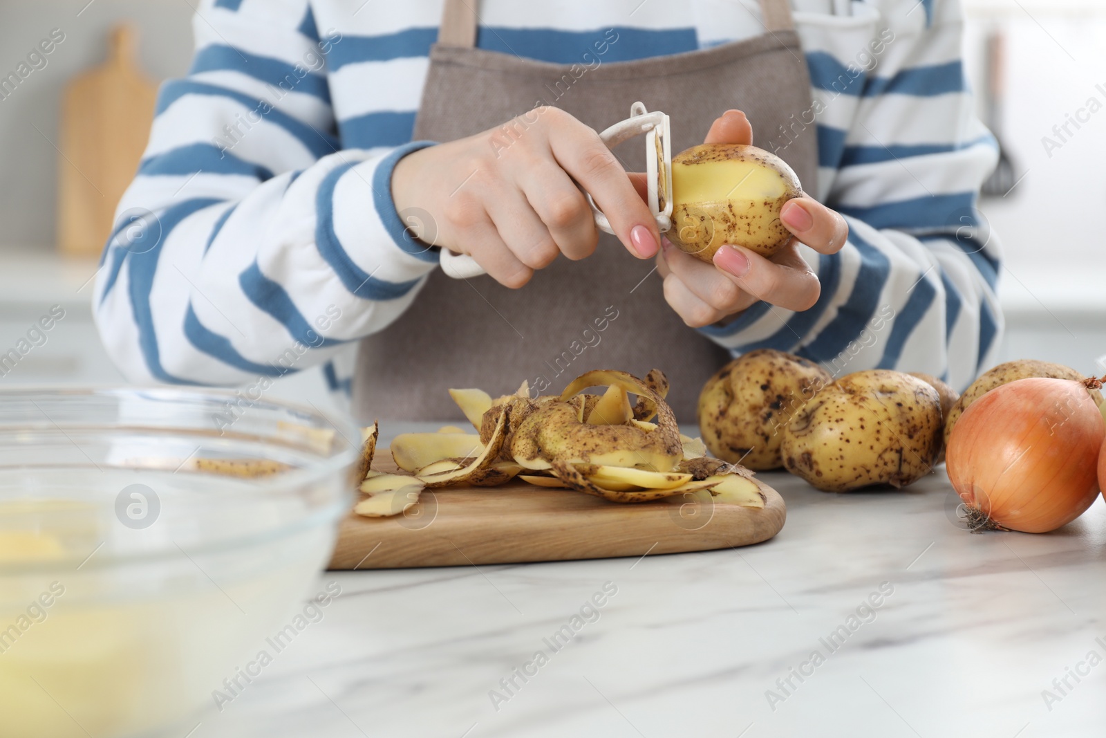 Photo of Woman peeling fresh potato at white marble table indoors, closeup