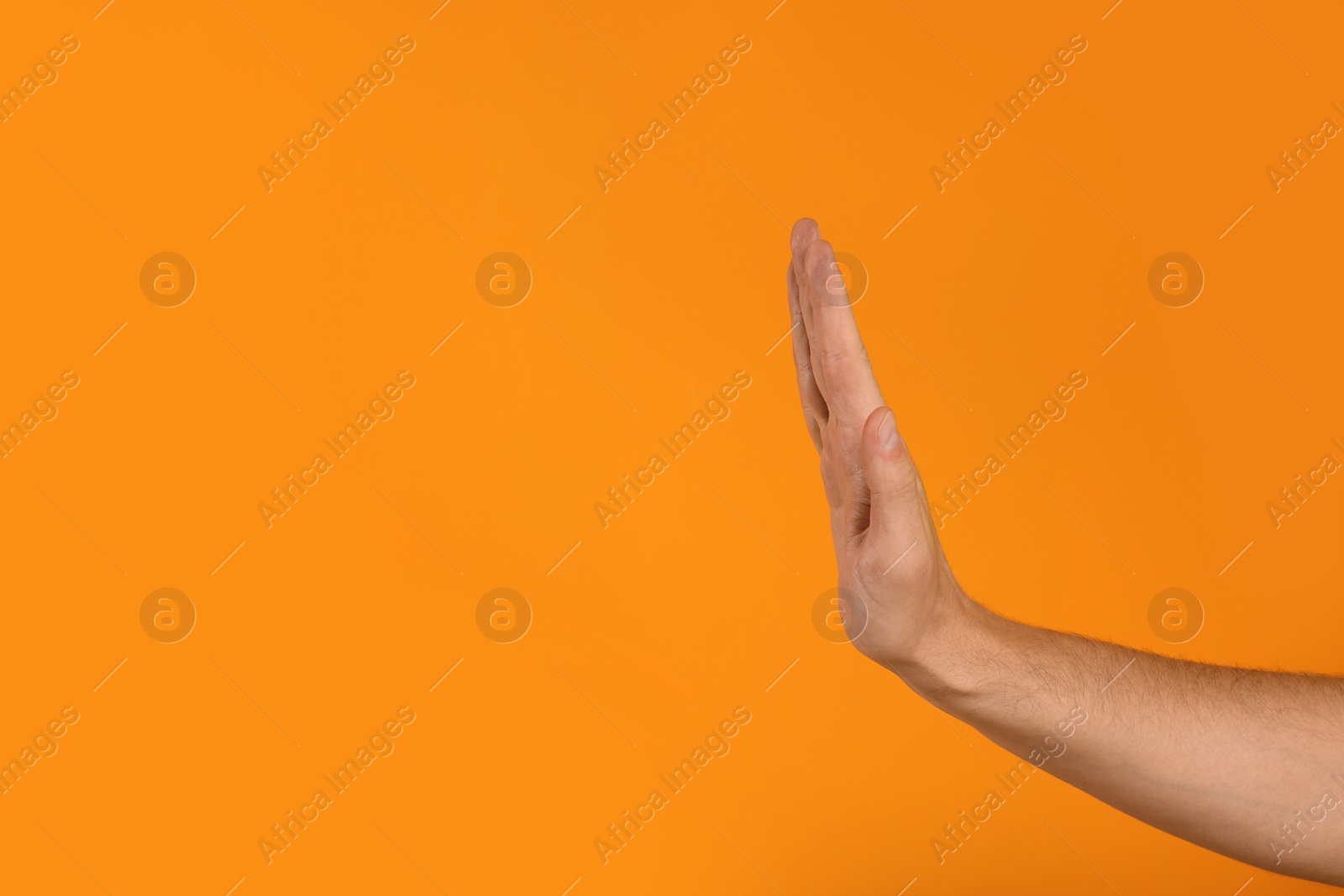 Photo of Man showing stop gesture on orange background, closeup with space for text