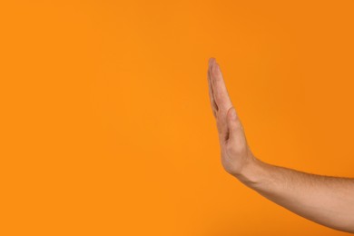 Photo of Man showing stop gesture on orange background, closeup with space for text
