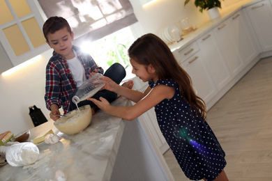 Photo of Cute little children cooking dough in kitchen at home