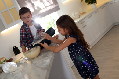 Cute little children cooking dough in kitchen at home