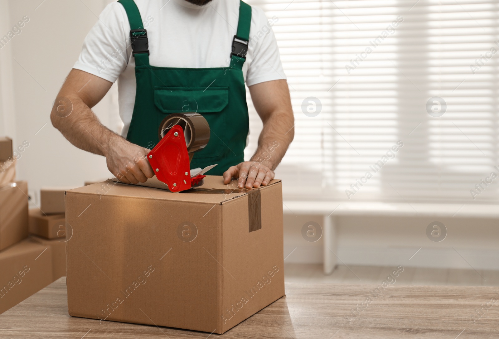 Photo of Man packing box with adhesive tape indoors, closeup. Moving service